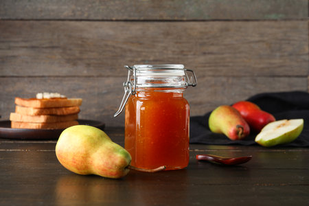 Glass jar of tasty pear jam on wooden backgroundの写真素材