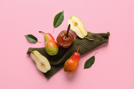Glass jar of tasty pear jam with towel on pink backgroundの写真素材