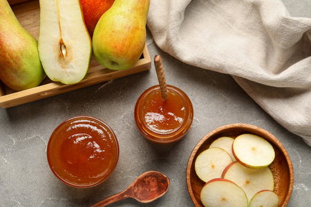 Glass jar and bowl of tasty pear jam with wooden box on gray tableの写真素材