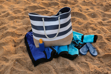 Stylish beach bag, flip-flops, sunscreen cream and towel on sandの写真素材