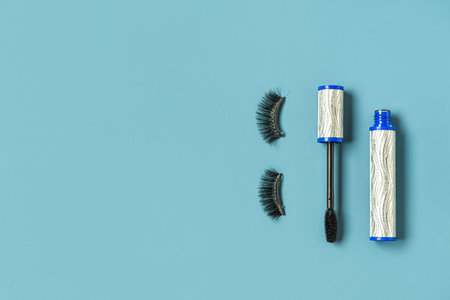 Black mascara in silver tube and fake eyelashes on blue background