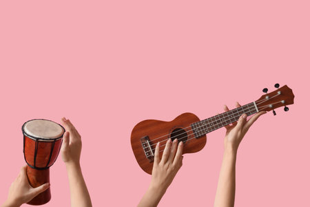 Female hands holding ukulele and drum on pink background