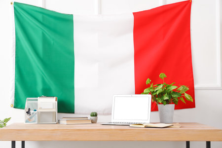Modern workplace with laptop, stationery and hanging Italian flag in office, closeupの写真素材