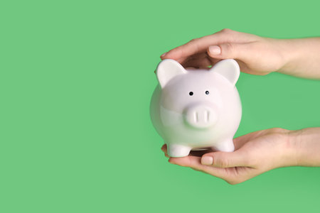 Female hands holding piggy bank on green backgroundの写真素材