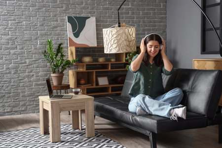 Young woman listening to music on sofa in living roomの写真素材