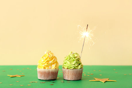 Tasty birthday cupcakes with sparkler and decor on color backgroundの写真素材