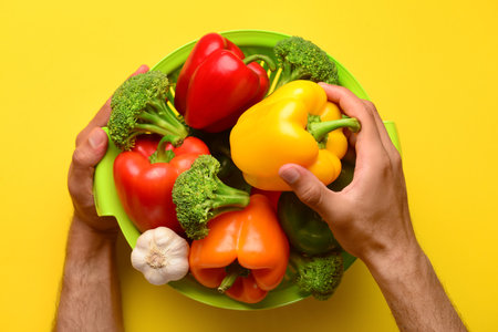 Man putting bell pepper into colander with different fresh vegetables on yellow backgroundの写真素材