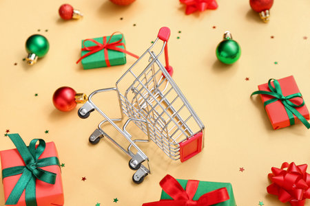 Composition with small shopping cart, Christmas balls and gift boxes on beige background, closeupの写真素材