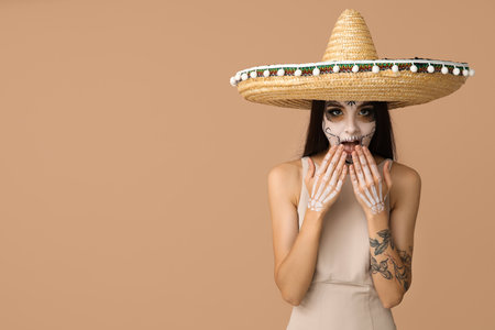 Shocked young woman dressed as dead bride for Halloween party in sombrero hat on beige backgroundの写真素材