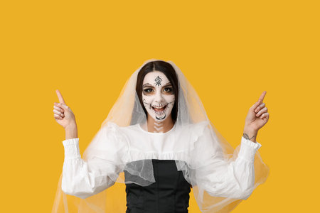 Beautiful young woman dressed as dead bride for Halloween party pointing at something on yellow...