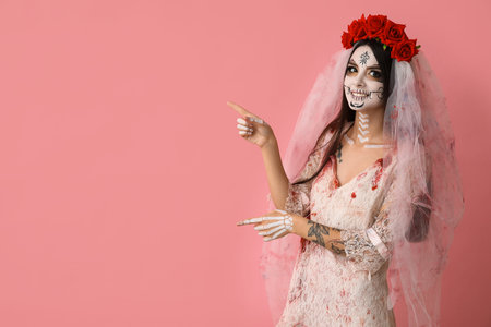 Beautiful young woman dressed as dead bride for Halloween party pointing at something on pink...