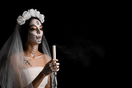 Young woman dressed as dead bride for Halloween party holding candlestick with candle on black...