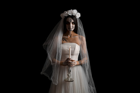 Young woman dressed as dead bride for Halloween party holding candlestick with candle on black...