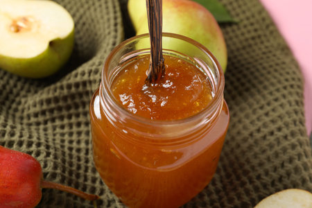 Glass jar of tasty pear jam on fabric backgroundの写真素材