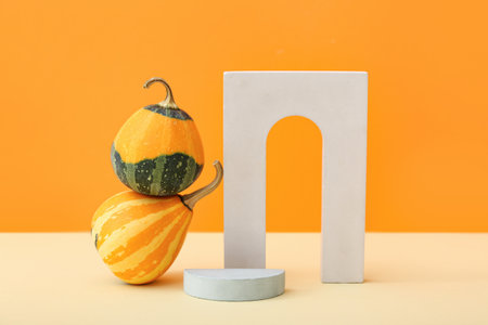 Decorative plaster podiums and pumpkins on beige table against orange backgroundの写真素材