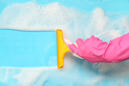 Female hand in rubber glove cleaning blue surface with squeegeeの写真素材