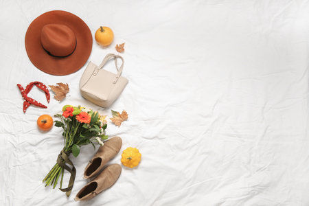 Beautiful autumn composition with stylish clothes, leaves, pumpkins and bouquet of flowers on white bed sheetの写真素材