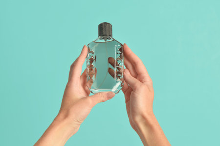Female hands with bottle of luxury perfume on turquoise background