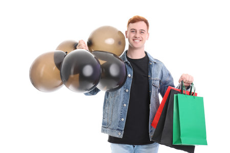 Happy young redhead man with shopping bags and balloons isolated on white background. Black Friday saleの写真素材