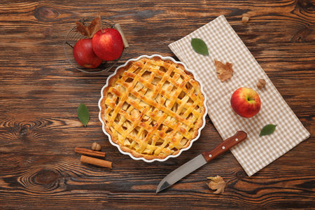 Baking dish with delicious apple pie and cinnamon on wooden backgroundの写真素材