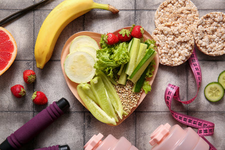 Plate with fresh healthy products and dumbbells on gray tile background. Diet conceptの写真素材