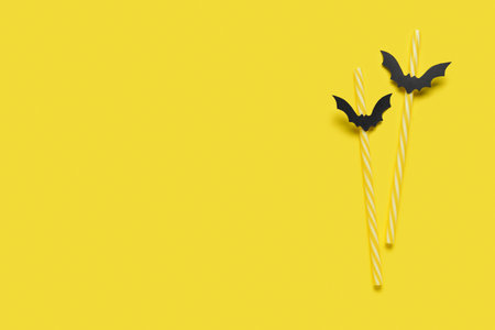 Drinking straws with paper bats for Halloween celebration on yellow backgroundの写真素材