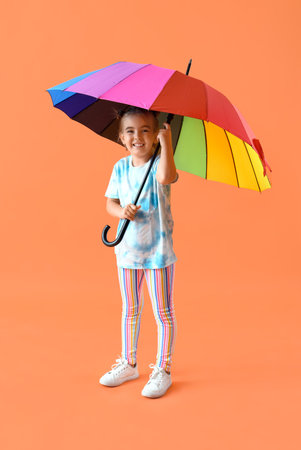 Cute little girl with umbrella on orange backgroundの写真素材