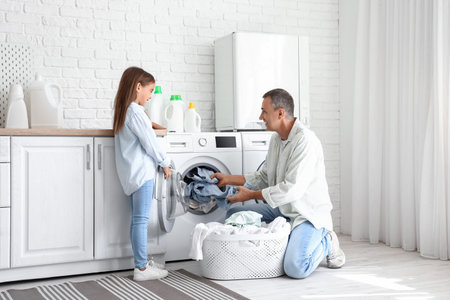 Mature man with his little granddaughter doing laundry at homeの写真素材