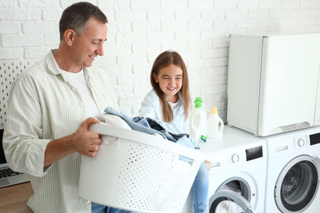 Mature man with laundry basket and his little granddaughter at homeの写真素材