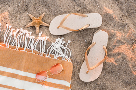 Stylish female flip flops, towel, sunglasses and starfish on sand