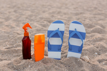 Stylish female flip flops and bottles of sunscreen on sandの写真素材