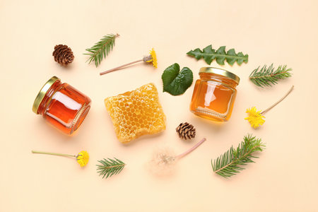 Jars with tasty honey, honeycomb, dandelion flowers and fir tree branches on beige backgroundの写真素材