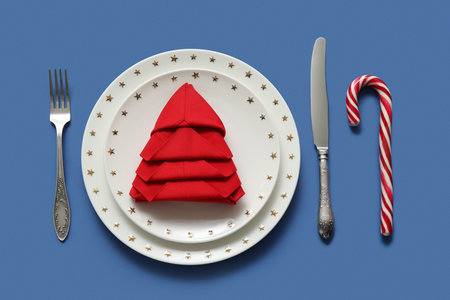 Festive table setting with folded napkin and Christmas decorations on blue background, closeupの写真素材