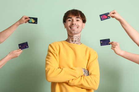 Tattooed young man and hands with credit cards on green background