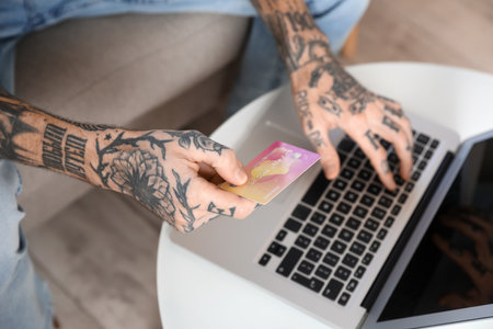 Tattooed young man with credit card using laptop at home, closeupの写真素材