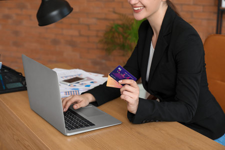 Young businesswoman with credit cards using laptop at table in office, closeupの写真素材