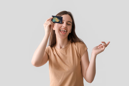 Young woman with credit card showing tongue on light backgroundの写真素材
