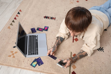 Tattooed young man with credit card using mobile phone at homeの写真素材