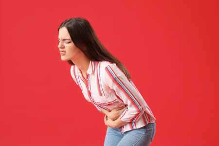 Young woman suffering from stomach ache on red backgroundの写真素材