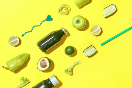 Bottles of healthy green juice with ingredients on yellow background
