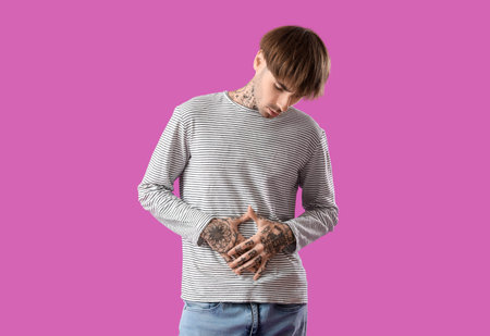Young man suffering from stomach ache on purple background