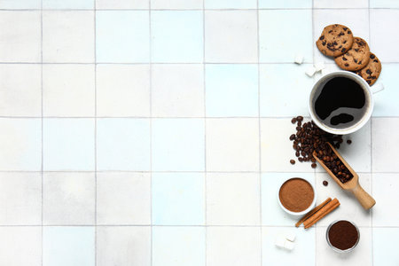Cup of tasty coffee with cinnamon, beans and cookies on white tile backgroundの写真素材