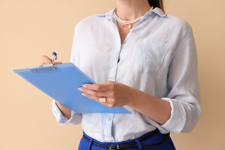 Beautiful businesswoman writing in clipboard on beige background, closeupの写真素材