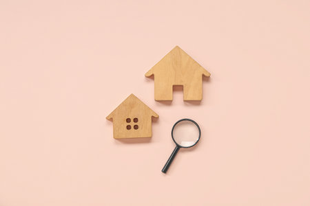 Wooden house figures with magnifier on pink background. Concept of buying real estateの写真素材