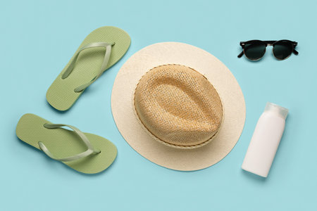 Straw hat, flip-flops, sunglasses and bottle of sunscreen cream on color background