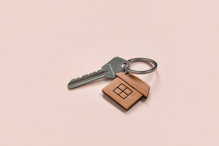 Key with trinket in house shape on pink background. Concept of buying real estate