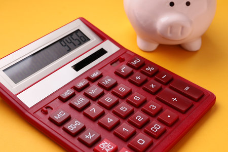 Red calculator and piggy bank on orange backgroundの写真素材