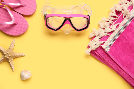 Swimming mask, flip flops, towel and seashell on yellow backgroundの写真素材