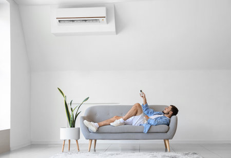 Young man switching on air conditioner at homeの写真素材