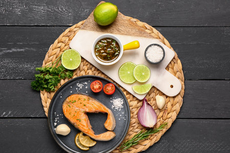 Plate of tasty salmon steak with vegetables and lime on black wooden backgroundの写真素材